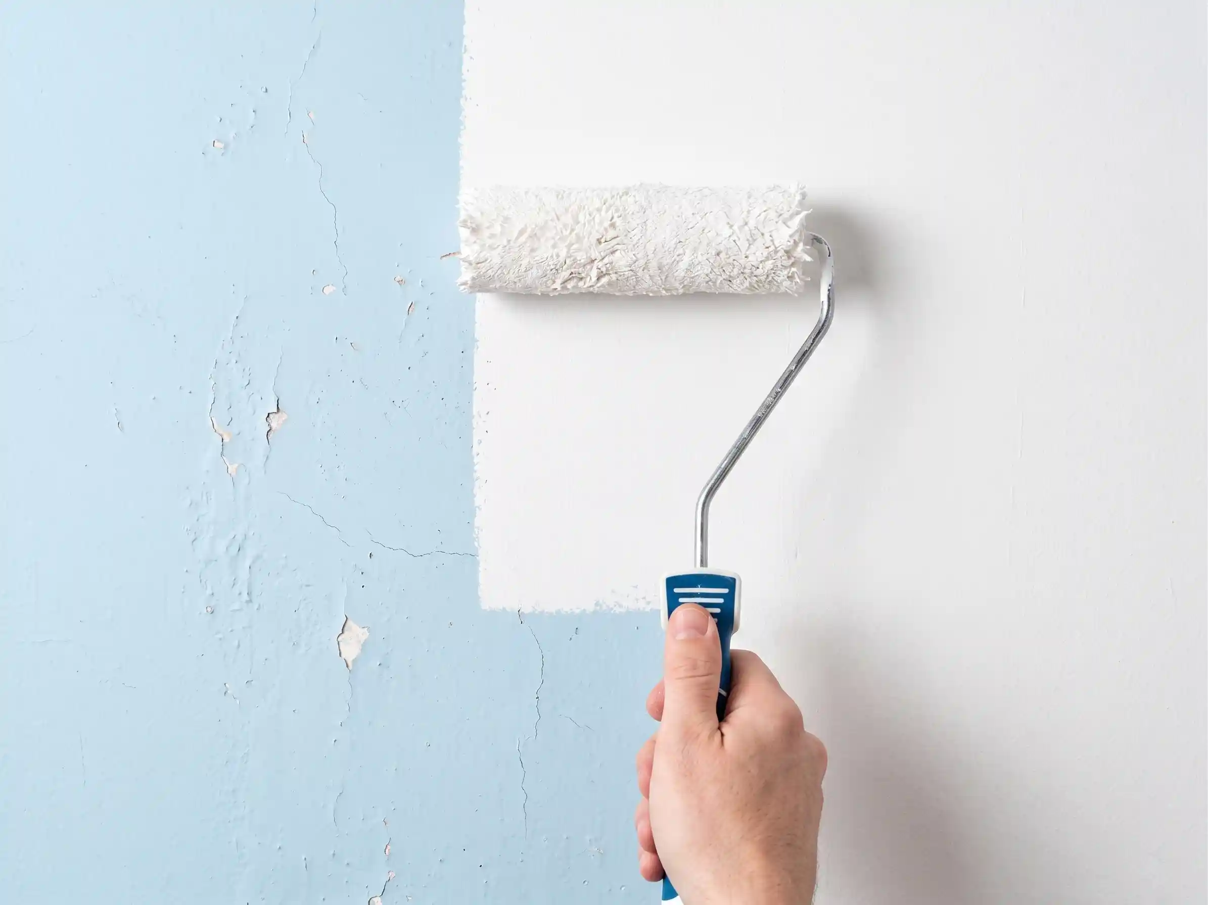 Rodillo aplicando pintura blanca en la pared de una vivienda en Elche